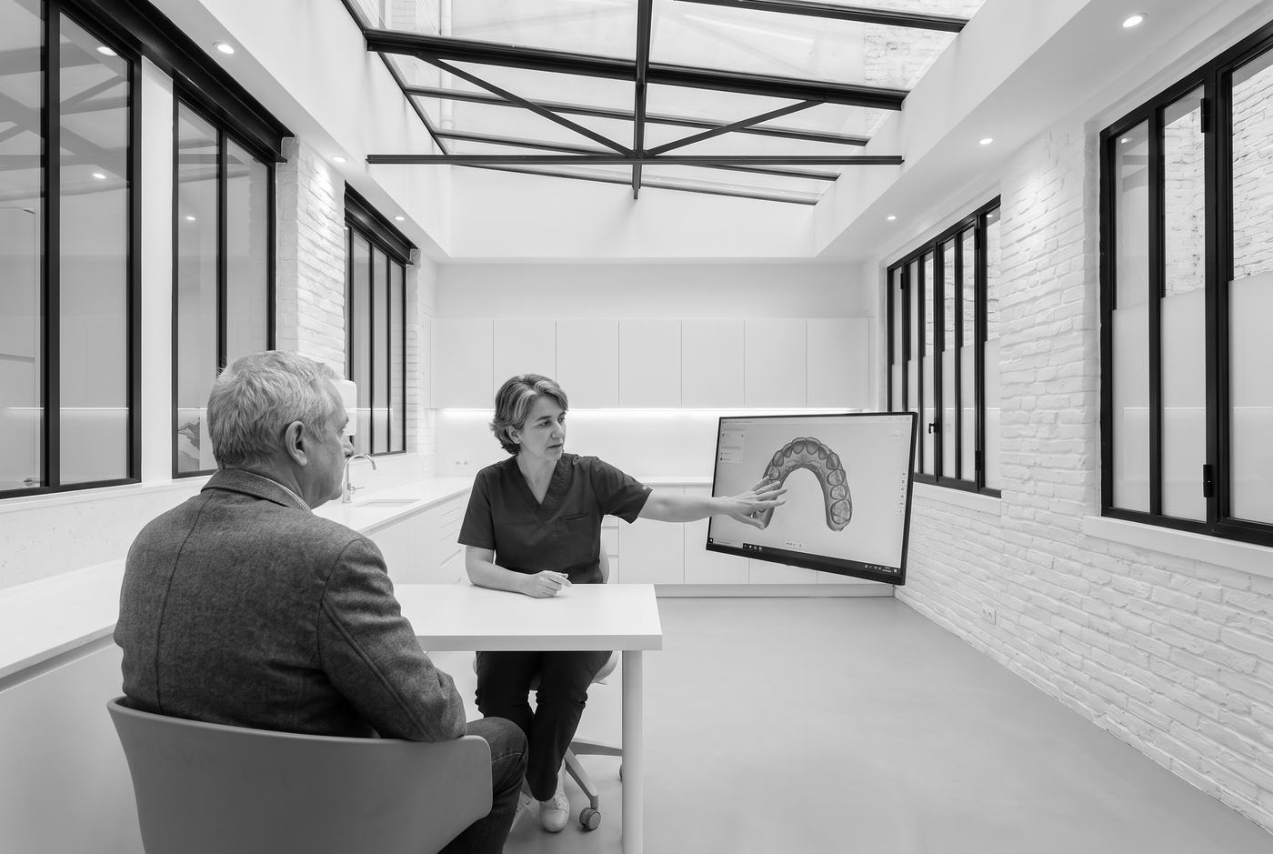 Une praticienne explique un soin à un patient en lui montrant ses dents en 3D à l'écran