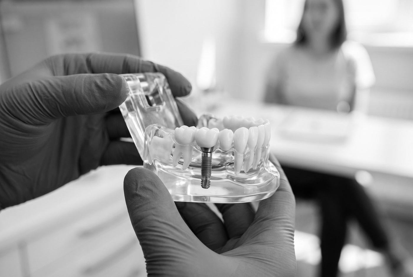 Des mains gantées tiennent une maquette de mâchoire avec un implant et sa couronne
