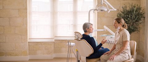Le Dr Juliette Brémond, assise à côté du fauteuil dentaire, écoute une patiente qui lui parle avant le soin