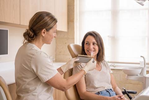 Le Dr Brémond compare la teinte des dents d'une patiente au nuancier, à la lumière du jour